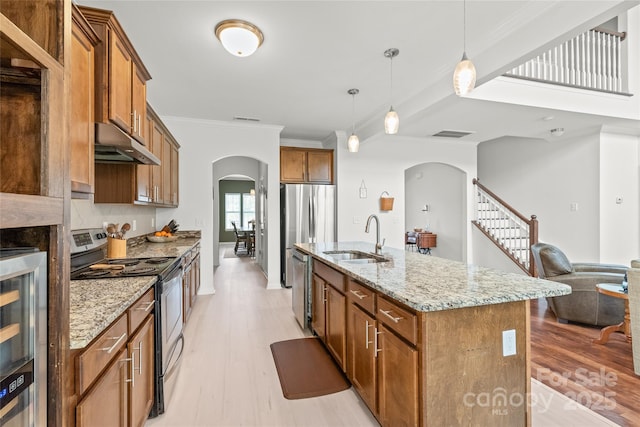 306 Fesperman Cir, Troutman, NC 28166 - kitchen featuring stainless steel appliances, arched walkways, under cabinet range hood, light wood-style floors, and brown cabinets