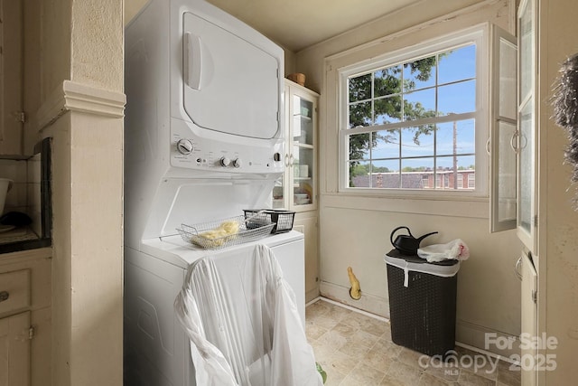 clothes washing area featuring baseboards, stacked washer / dryer, and laundry area