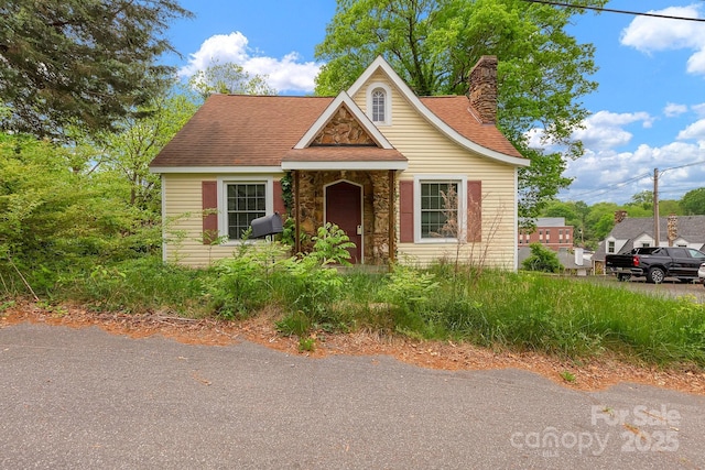bungalow with a chimney, roof with shingles, and stone siding