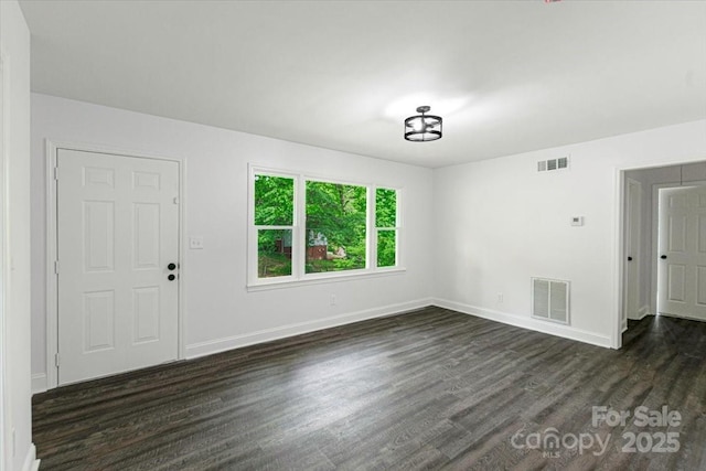 spare room featuring visible vents, baseboards, and dark wood-style flooring