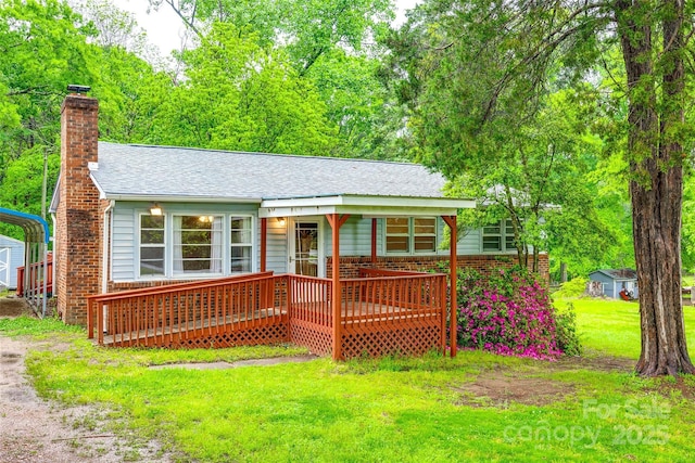 rear view of house with driveway, a carport, a chimney, roof with shingles, and a lawn