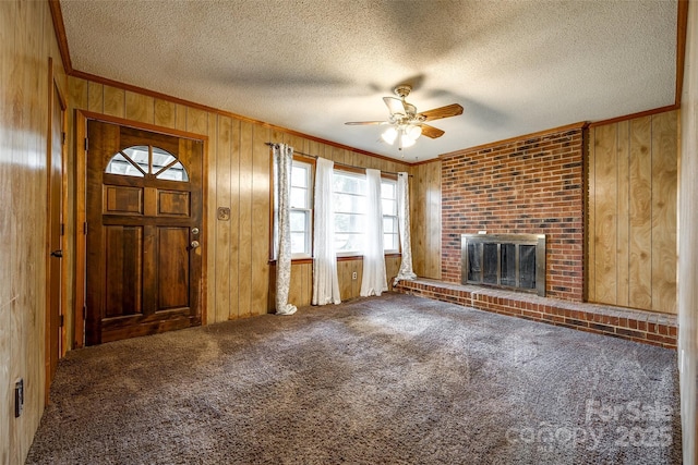 unfurnished living room featuring wood walls, ceiling fan, a fireplace, and crown molding