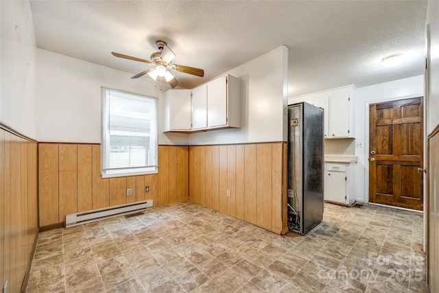 kitchen with freestanding refrigerator, wainscoting, a baseboard heating unit, a ceiling fan, and wooden walls
