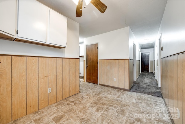 interior space featuring stone finish flooring, ceiling fan, attic access, wooden walls, and wainscoting