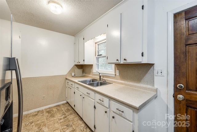 kitchen featuring light countertops, white cabinets, a sink, baseboards, and a textured ceiling