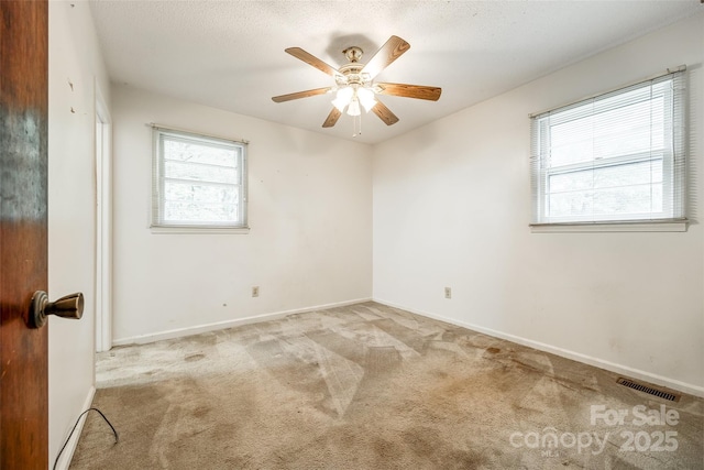 carpeted spare room featuring visible vents, a ceiling fan, and baseboards