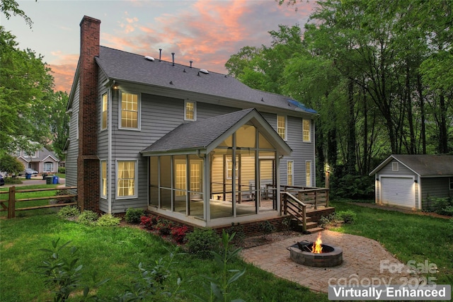 back of property with a sunroom, an outbuilding, a yard, a chimney, and a fire pit