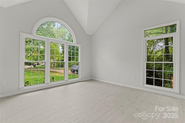 empty room featuring baseboards, light wood-style floors, and vaulted ceiling