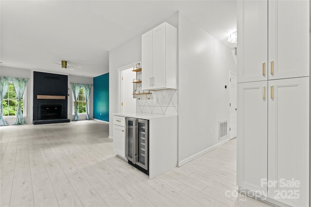kitchen featuring wine cooler, a large fireplace, visible vents, and white cabinets