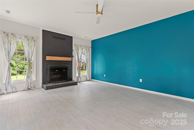 unfurnished living room with a brick fireplace, a healthy amount of sunlight, a ceiling fan, visible vents, and wood finished floors