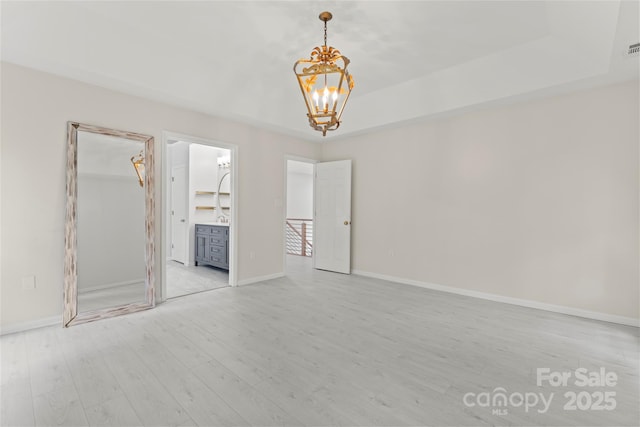 unfurnished bedroom with an inviting chandelier, a raised ceiling, light wood finished floors, and baseboards