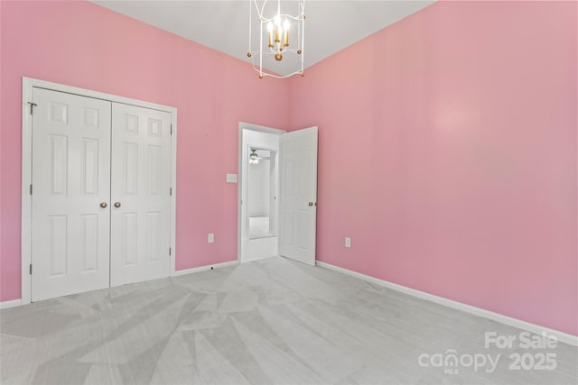 unfurnished bedroom featuring a closet, a notable chandelier, light colored carpet, and baseboards