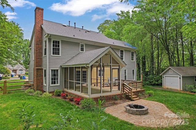 back of property with a sunroom, an outdoor fire pit, an outdoor structure, a yard, and a chimney