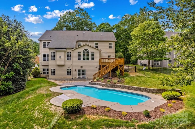 outdoor pool featuring a lawn, fence, a wooden deck, and stairs