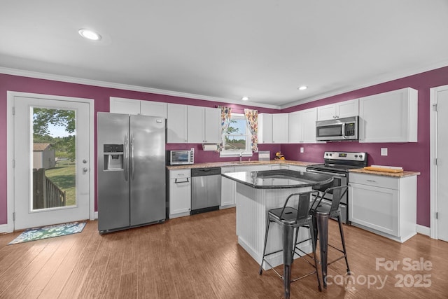 250 Log Barn Rd, Salisbury, NC 28146 - kitchen with crown molding, wood finished floors, a kitchen breakfast bar, white cabinetry, and appliances with stainless steel finishes