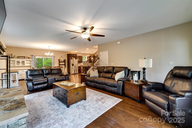 living area featuring stairway, dark wood-style floors, and ceiling fan with notable chandelier