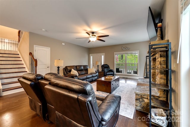 living room featuring dark wood-type flooring, a ceiling fan, and stairs