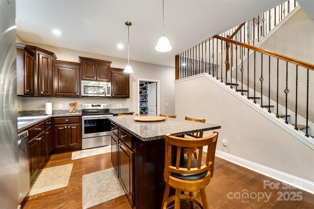 kitchen with dark wood-style flooring, dark brown cabinetry, a breakfast bar, stainless steel appliances, and a kitchen island