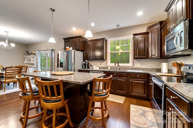 kitchen with a healthy amount of sunlight, dark brown cabinetry, a kitchen island, appliances with stainless steel finishes, and a sink