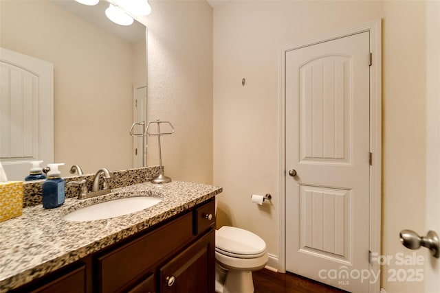 half bath featuring vanity, wood finished floors, and toilet