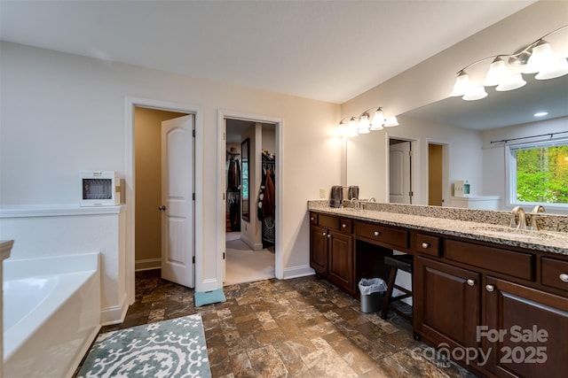 full bathroom with a walk in closet, a sink, double vanity, stone finish floor, and a bath