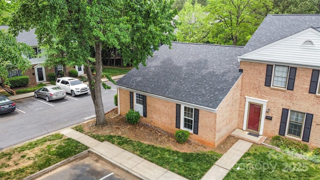 view of front of home with uncovered parking, roof with shingles, and brick siding