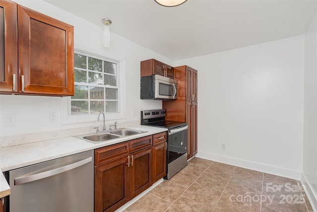 kitchen featuring stainless steel appliances, a sink, light countertops, baseboards, and brown cabinets