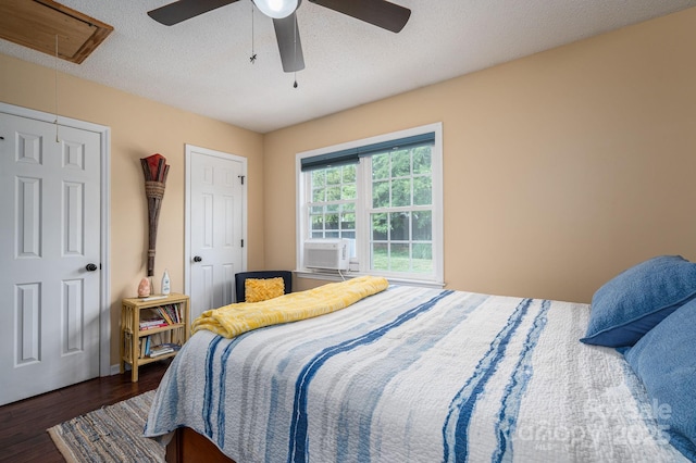 bedroom with a ceiling fan, a textured ceiling, attic access, and dark wood-type flooring
