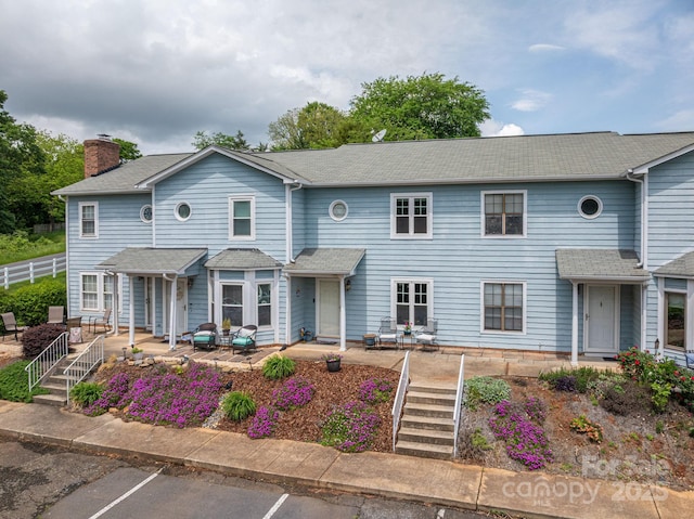 view of property with uncovered parking, a patio, a chimney, and roof with shingles