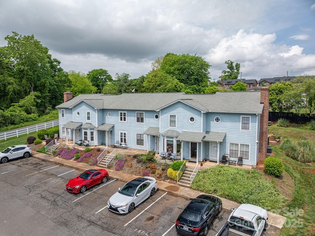 view of front of home with a shingled roof, uncovered parking, fence, and a chimney