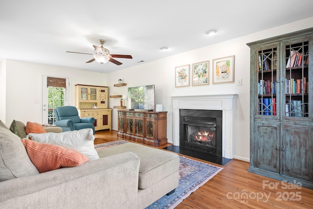 living room featuring a fireplace with flush hearth, wood finished floors, visible vents, and ceiling fan