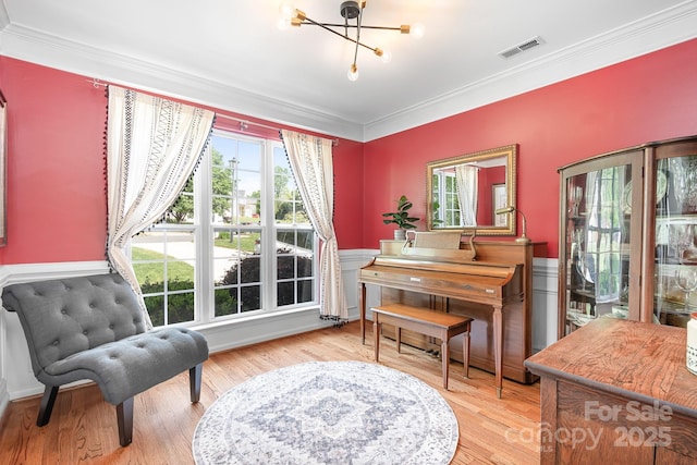 sitting room featuring crown molding, wood finished floors, a wainscoted wall, a notable chandelier, and visible vents