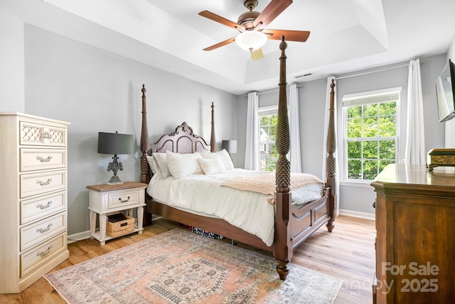 bedroom featuring light wood finished floors, baseboards, visible vents, ceiling fan, and a raised ceiling