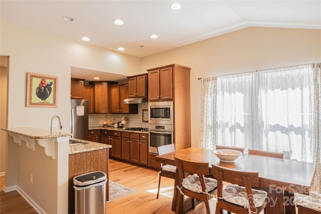 kitchen featuring tasteful backsplash, light stone countertops, appliances with stainless steel finishes, light wood finished floors, and a sink
