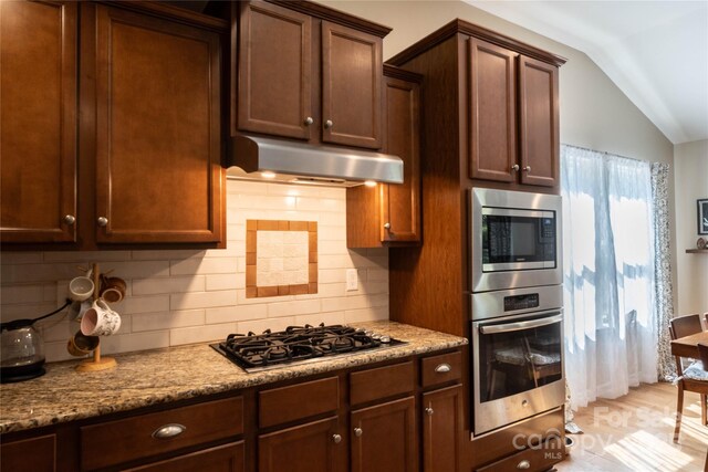 kitchen featuring tasteful backsplash, light wood-style flooring, under cabinet range hood, appliances with stainless steel finishes, and vaulted ceiling