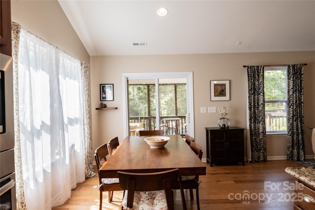 dining area with visible vents, a healthy amount of sunlight, light wood-style flooring, and vaulted ceiling