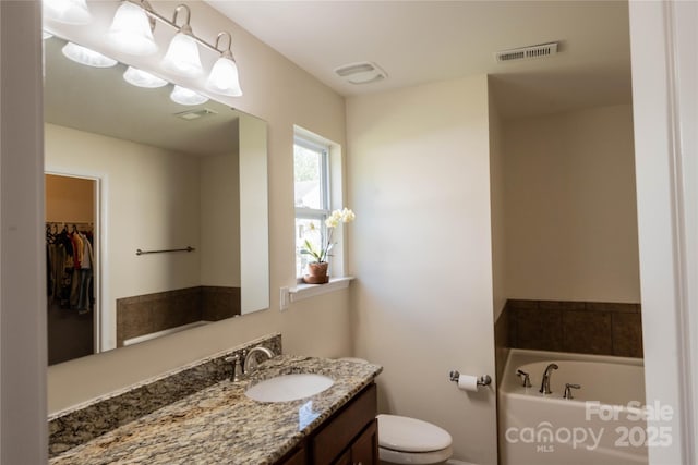 bathroom featuring toilet, visible vents, vanity, and a bath