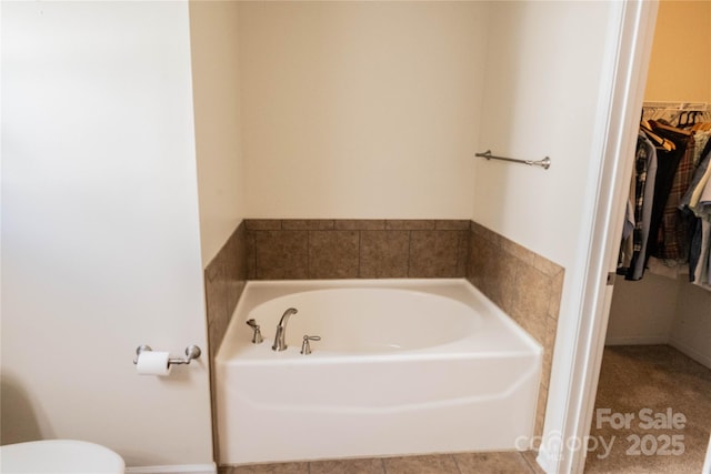 full bath featuring a walk in closet, toilet, tile patterned floors, and a garden tub