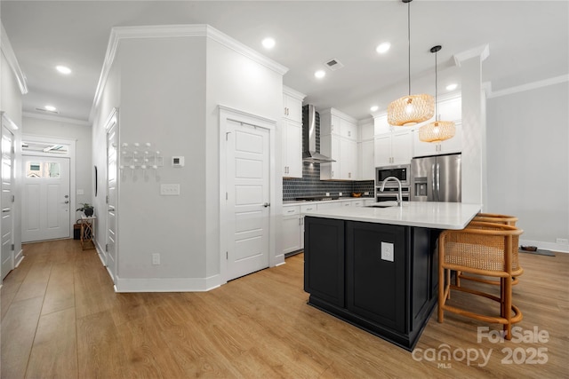 kitchen featuring wall chimney range hood, visible vents, light countertops, a sink, and stainless steel appliances