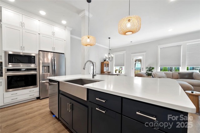 kitchen with crown molding, appliances with stainless steel finishes, a sink, open floor plan, and white cabinetry