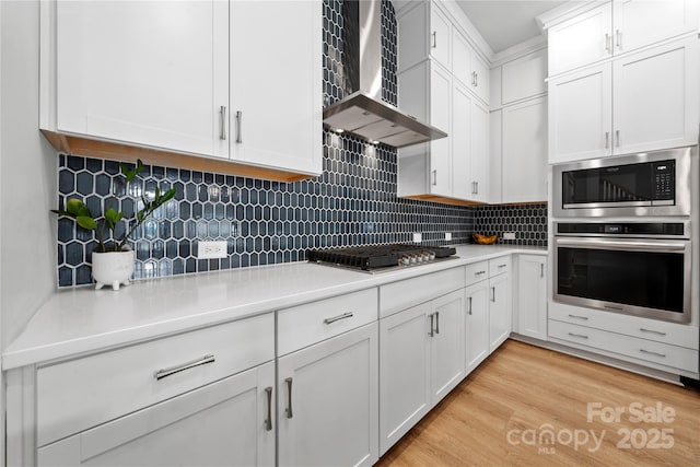 kitchen featuring light countertops, white cabinets, stainless steel appliances, and wall chimney exhaust hood