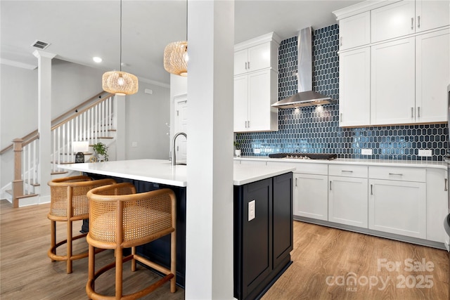 kitchen featuring crown molding, light wood-style floors, wall chimney exhaust hood, visible vents, and stovetop