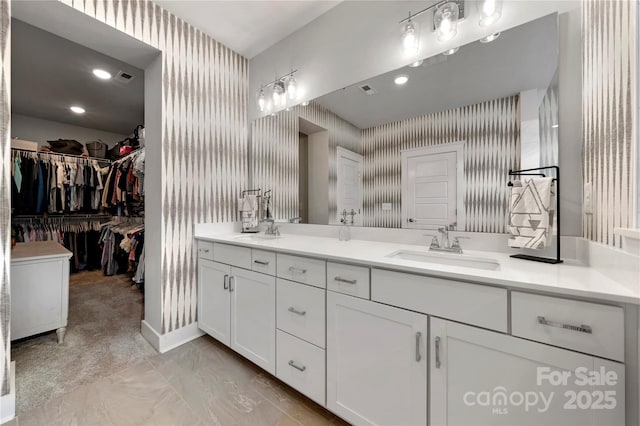 full bathroom featuring double vanity, a sink, a spacious closet, and wallpapered walls