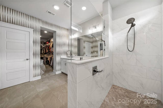 full bathroom featuring visible vents, a tile shower, a spacious closet, and vanity