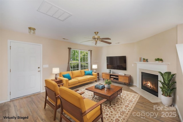 living area featuring a ceiling fan, visible vents, a glass covered fireplace, and light wood-style floors