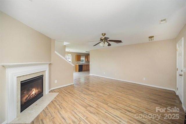 unfurnished living room featuring visible vents, a fireplace, light wood-style floors, baseboards, and ceiling fan