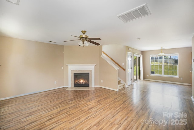 unfurnished living room with visible vents, stairs, light wood-type flooring, a high end fireplace, and a ceiling fan