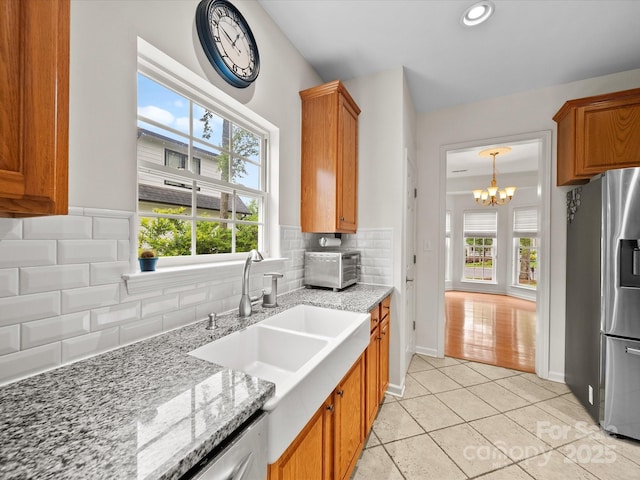 kitchen with light stone counters, a sink, a notable chandelier, brown cabinetry, and stainless steel fridge with ice dispenser