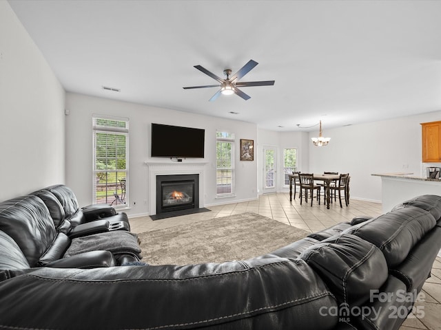 living area featuring a fireplace with flush hearth, visible vents, plenty of natural light, and ceiling fan with notable chandelier