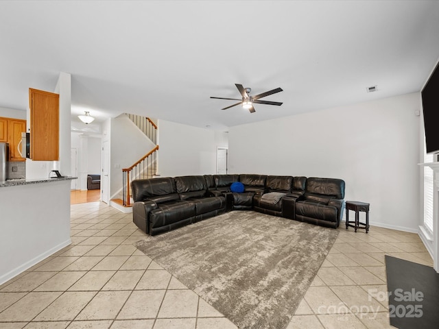 living area with light tile patterned flooring, a ceiling fan, stairs, visible vents, and baseboards
